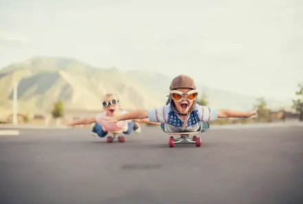 Zwei Kinder fahren auf dem Bauch liegend auf einem Skateboard