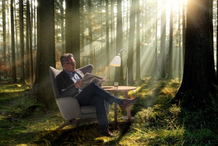 Mann im Ohrensessel liest Zeitung im Wald